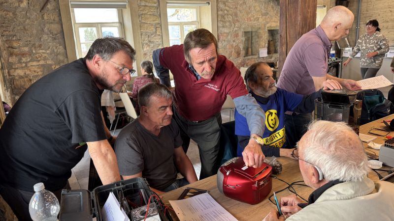 Das Bild zeigt mehrere Personen die beratend ein defekte Gerät begutachten.